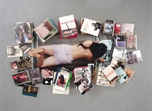 This may contain: a woman laying on the ground surrounded by many books