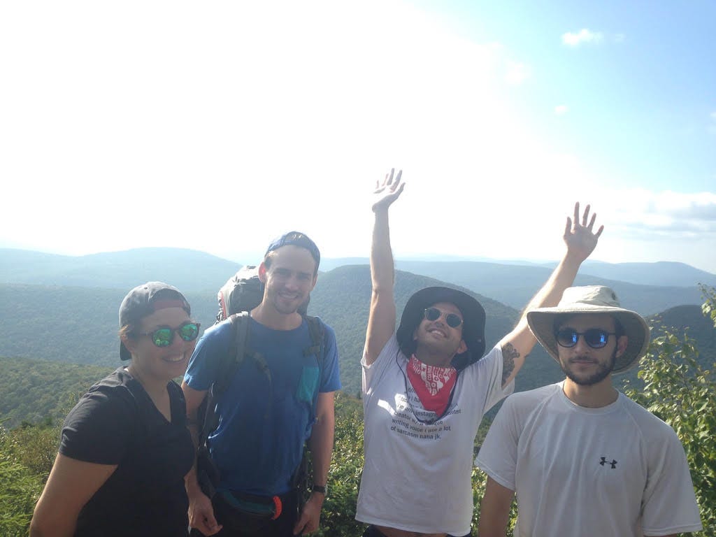 four people standing on top of a mountain with lower mountains in the background. the sun is behind them. four people standing on top of a mountain with lower mountains in the background. the sun is behind them.