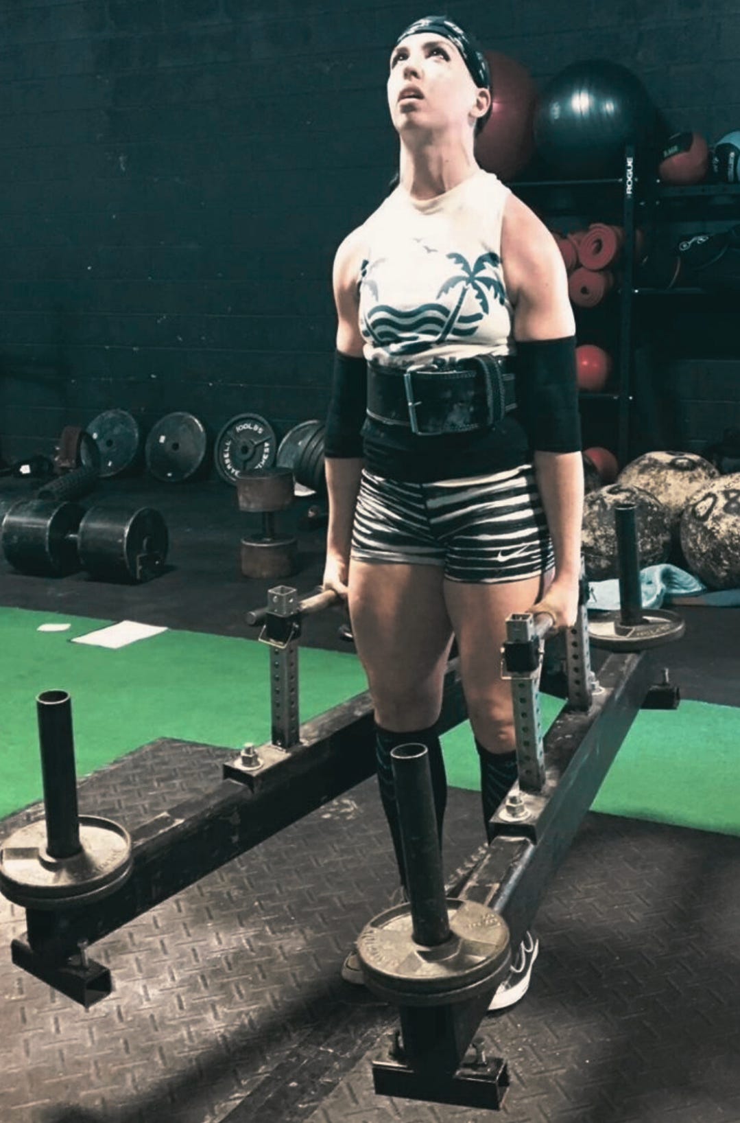 The author stands under a harsh overload light and gazes up, their entire body tense from the long loaded handles they grasp in each hand.