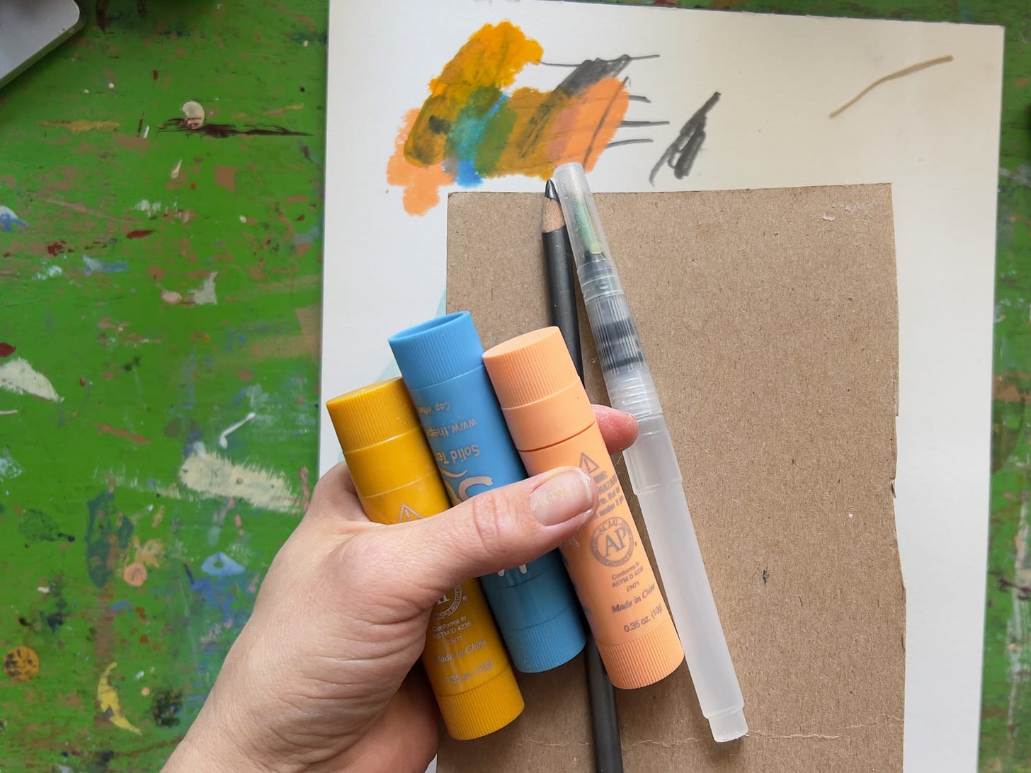 paint sticks, waterbrush, and pencil over a swatch of colors