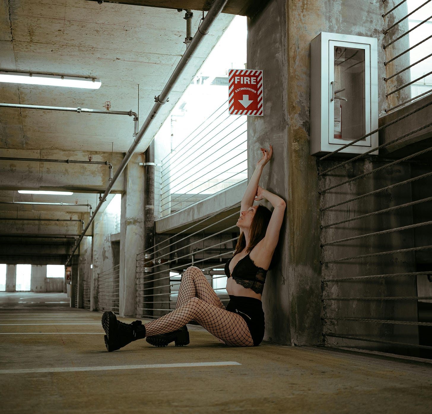 Woman in fishnet stockings, black shorts, black bra in empty parking garage