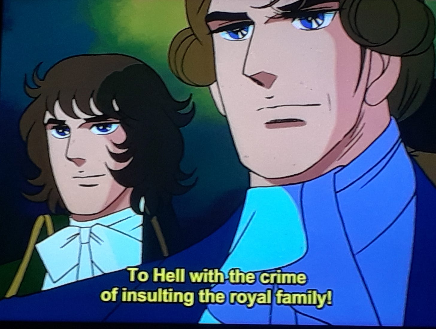 Two men stand side-by-side, one with brown hair and blue eyes in the background, and another, Robespierre, with his carefully crofted brown hair, possibly a wig, his face and neck gallantly looking ahead in the foreground. At the bottom of the screen reads the words, in yellow type, "To Hell with the crime of insulting the royal family!"