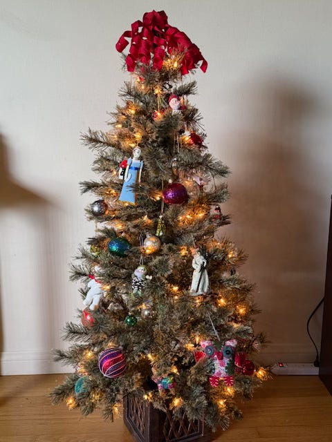 A small Christmas tree decorated with white lights and assorted ornaments and colored balls, a curly red ribbon spiraling off the top.