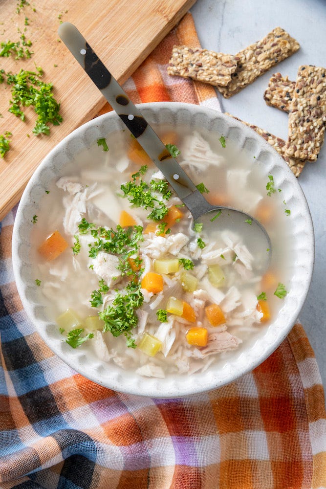 Chicken soup in a white bowl and three plates of potato latkes