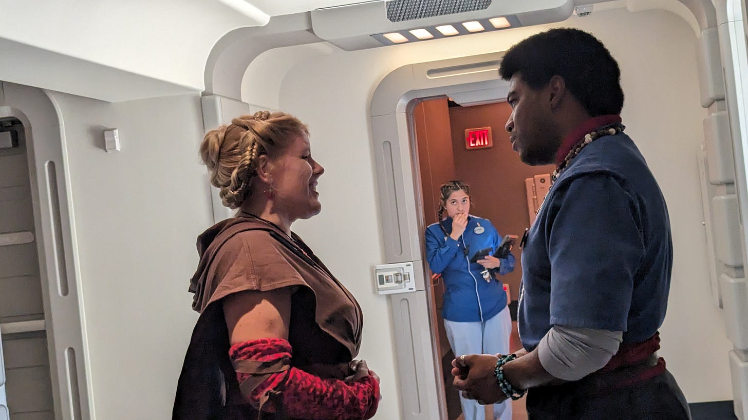 Cass talking to Saja Tycer in a corridor of the Halcyon, with another blueshirt crew member in the background