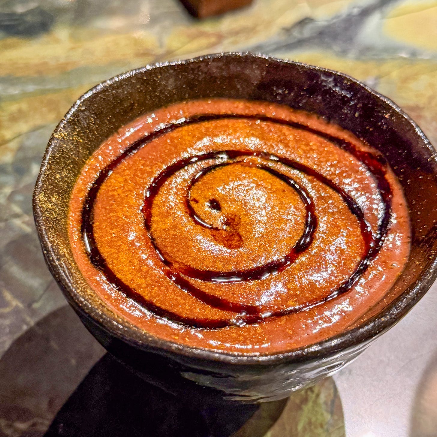 Chocolate mousse with dark syrup spiral pattern in ceramic bowl at Mantra restaurant