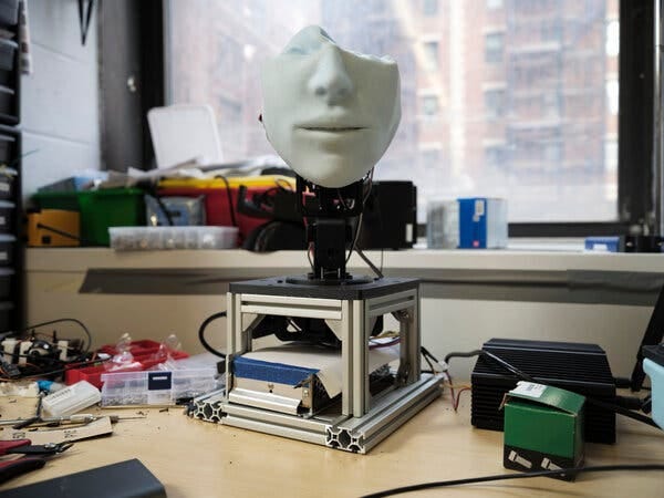A close-up view of another robot face on a metal stand. Only the bottom half of the face has been fitted over machinery, so it looks as though the top half has collapsed and it has no eyes.