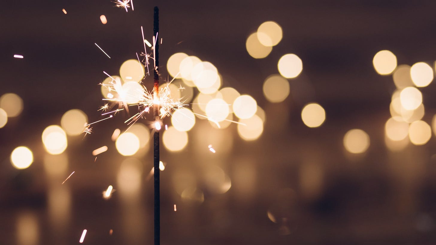 Close-up sparks of a sparkler, wire inside glowing red, blurry background full of dotted lights
