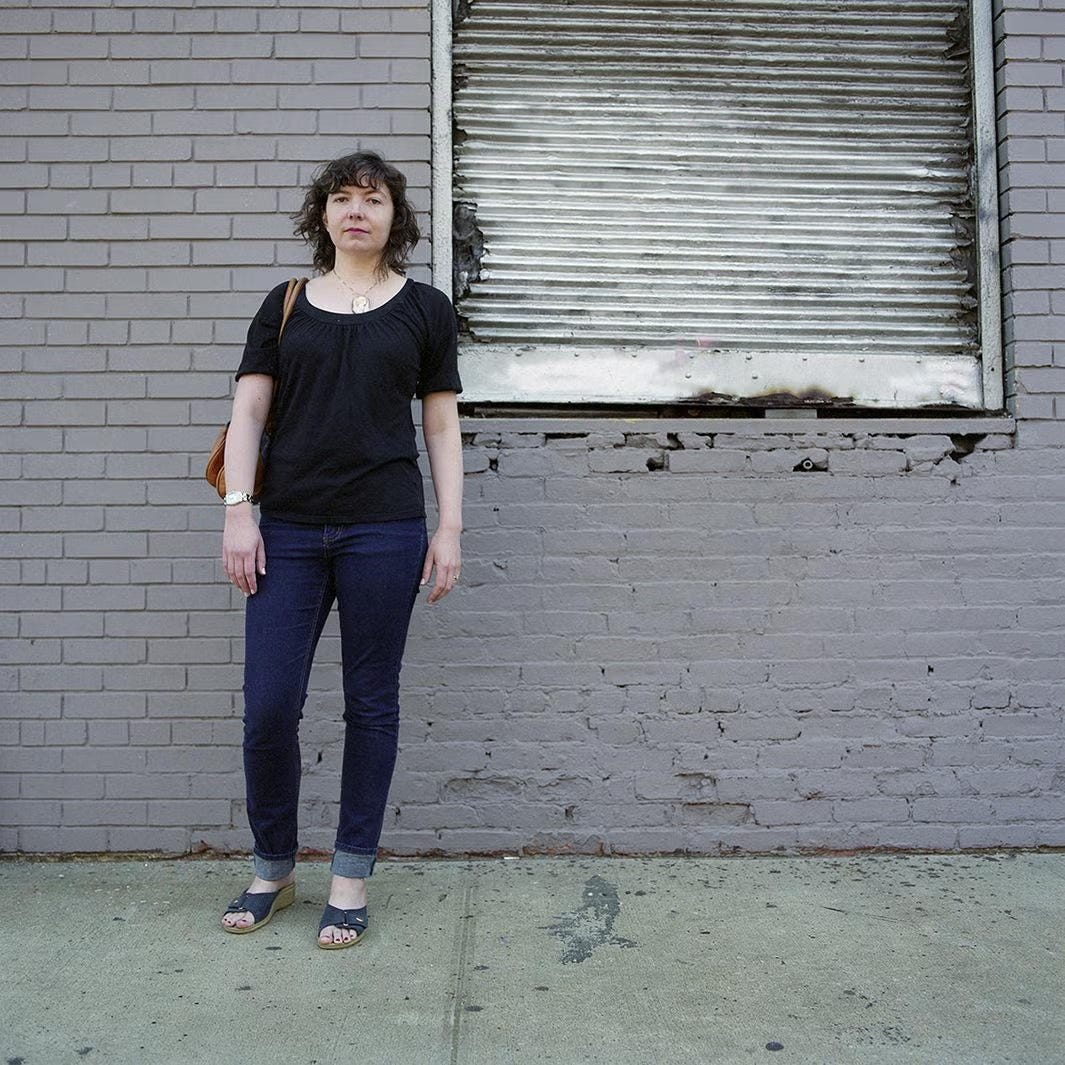 white woman in jeans with a purse and brown hair stands in front of a run down building white woman in jeans with a purse and brown hair stands in front of a run down building