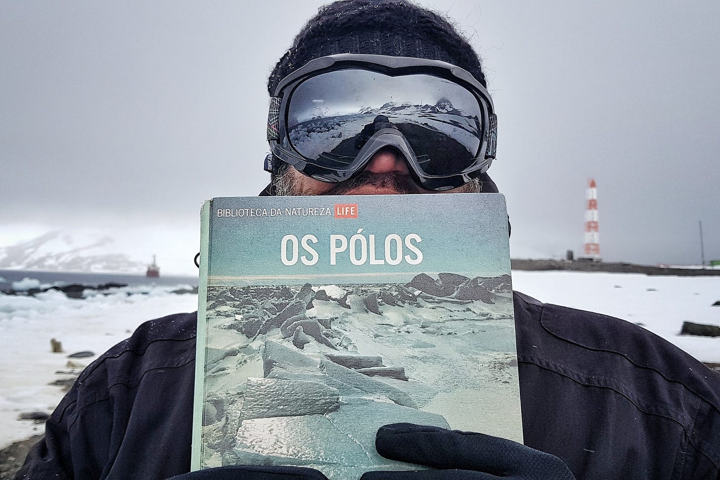Renato na Antártica, segurando um livro sobre "Os Polos"