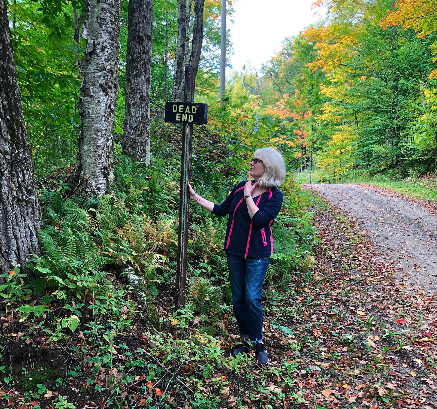 Woman standing on country road looking at a Dead End sign Woman standing on country road looking at a Dead End sign