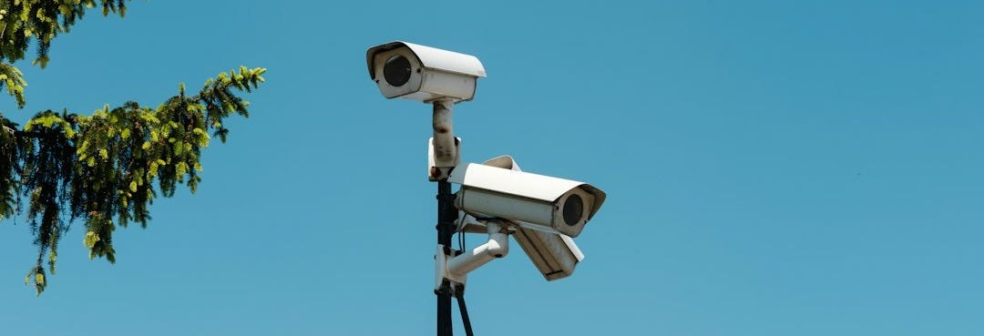 Two white security cameras mounted on a pole against a clear blue sky