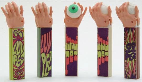 Five PEZ dispensers with psychedelic bodies which say Luv Pez, Mad Pez, and Go Go Pez. The top is a hand holding an eyeball. 