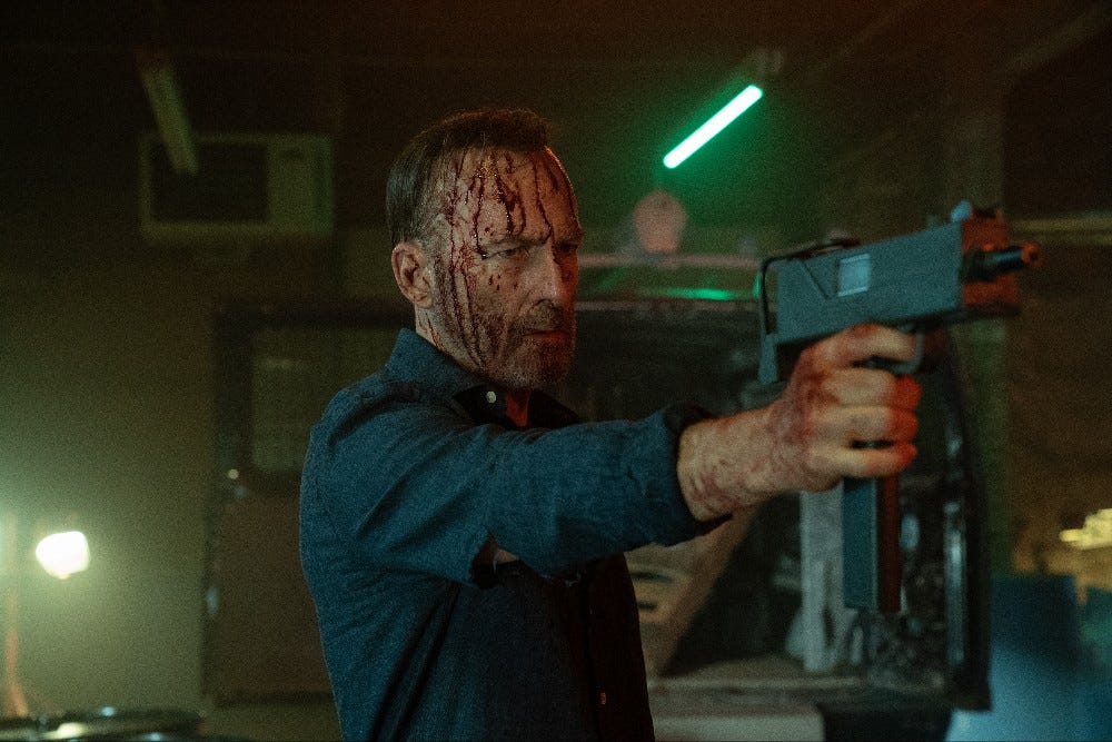 Bob Odenkirk in Nobody 2 holding a gun and covered in blood.