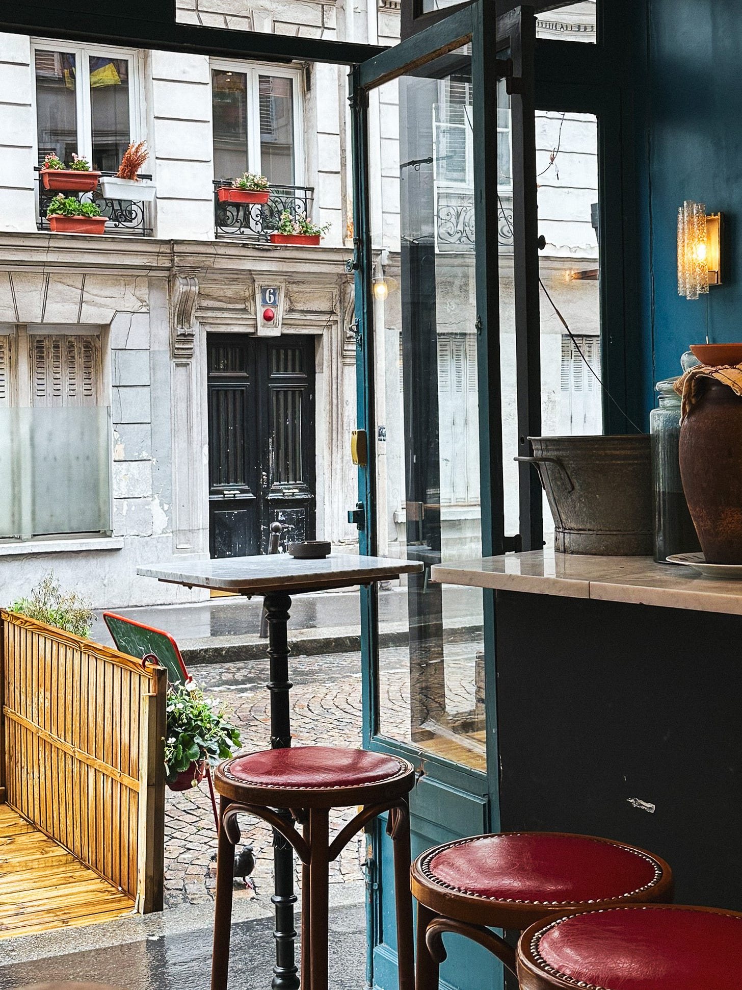 French wine bar with red leather stools, bold blue walls, overlooking a sleepy cobblestone street