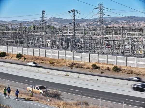 An electrical substation is surrounded by a concrete wall that faces a busy road. An electrical substation is surrounded by a concrete wall that faces a busy road.