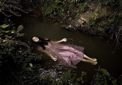 This may contain: a woman in a pink dress floating on top of a body of water surrounded by greenery