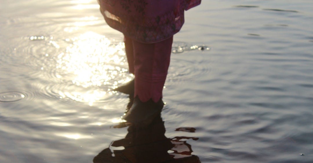 Legs wading in water, bright sun reflection on surface.
