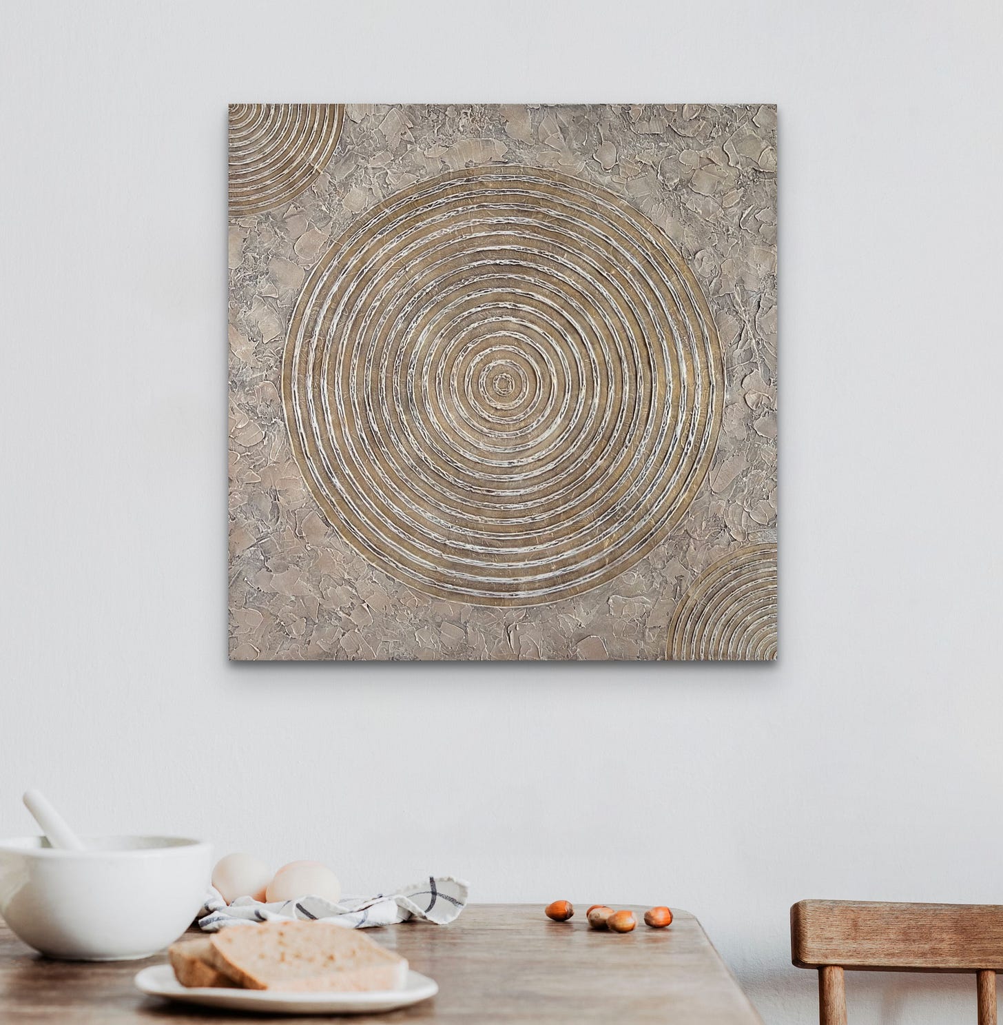 The abstract painting Morning Frost displayed in a cozy home setting. Its textured circular patterns in earthy, neutral tones complement the surrounding space, adding a quiet, grounding presence to the room.