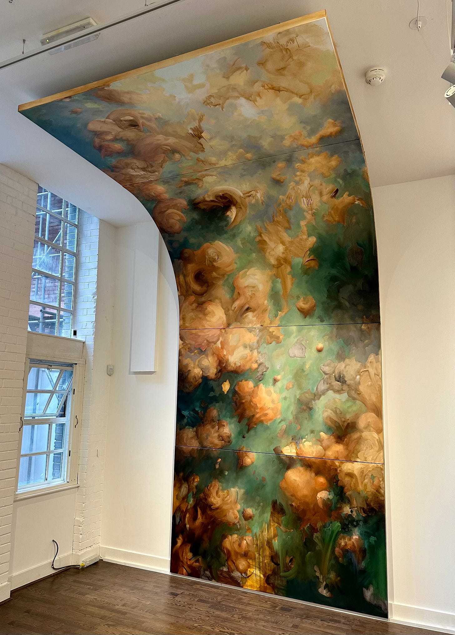 A giant canvas made up of four panels that reaches from floor to ceiling containing an abstract painting with green, yellow and brown cloud like formations in a white walled gallery. A giant canvas made up of four panels that reaches from floor to ceiling containing an abstract painting with green, yellow and brown cloud like formations in a white walled gallery.