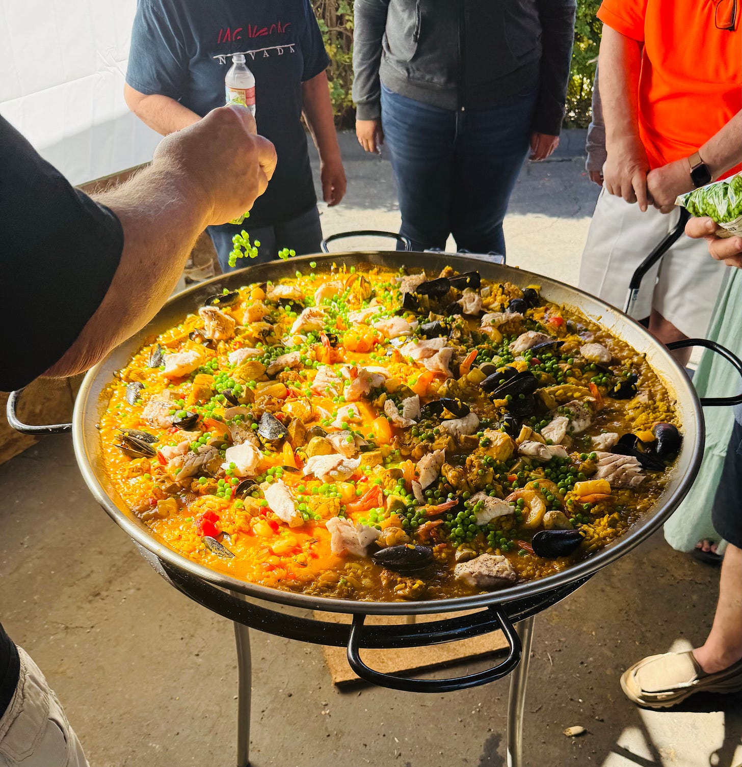 Peas being sprinkled into a pan of cooking paella