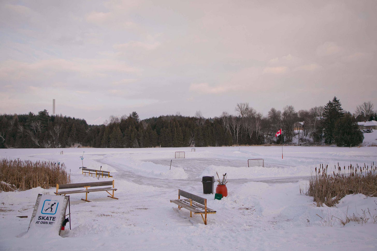 An empty skating pond with abandoned hockey sticks and a sign that says "Skate At Own Risk." Photo credit: Nancy Forde. nancyforde.com