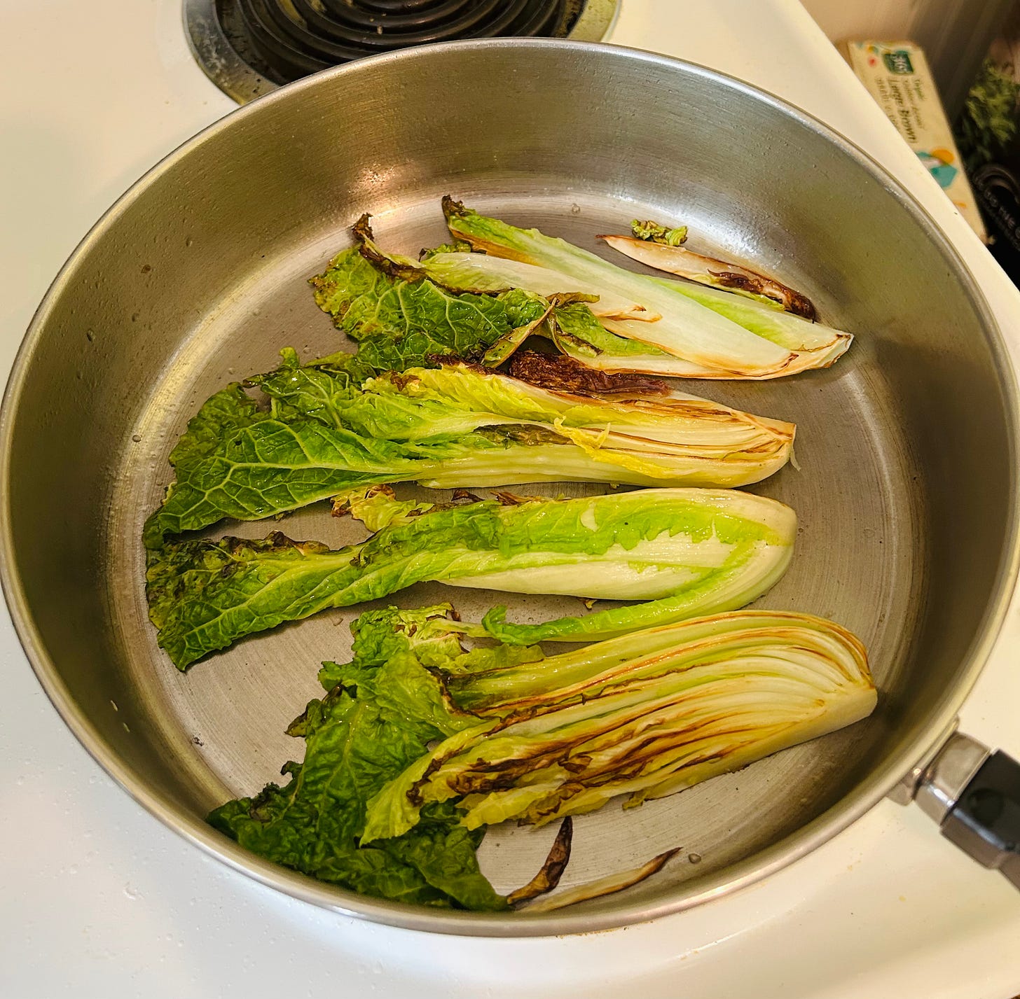 A frying pan holds bright green and yellow wedges of cabbage that are charred on some edges.