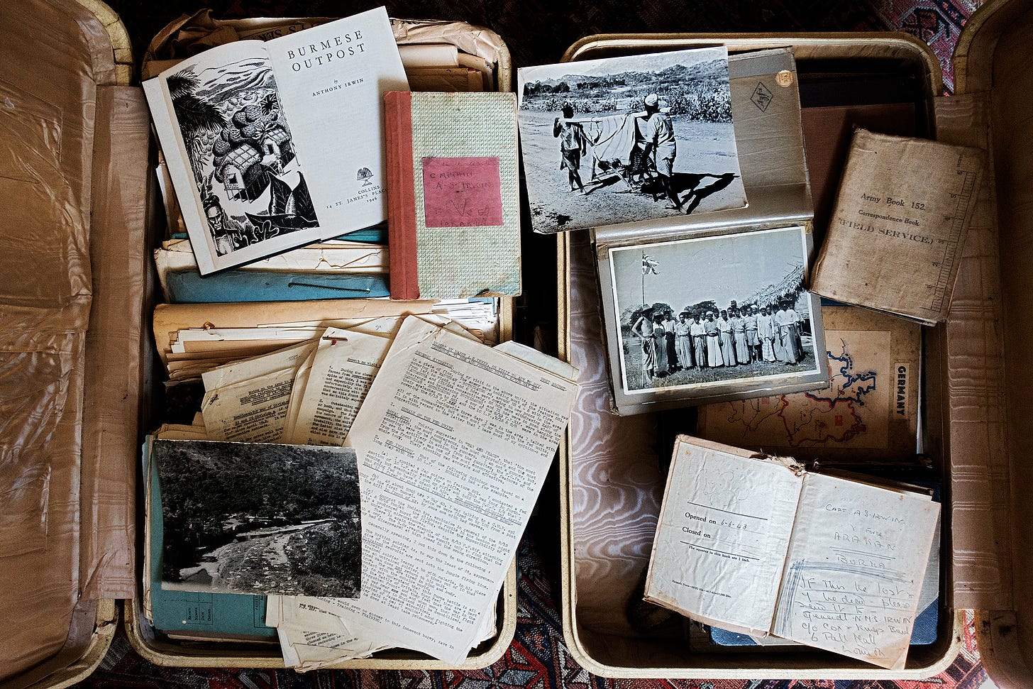 A picture, taken from above, of two old-looking suitcases. The suitcases are open and contain old documents, photos, notebooks, and files.