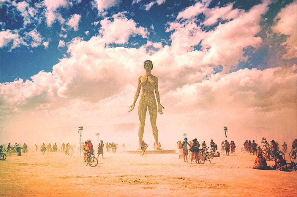 Picture of scultpure in middle of desert with people around it