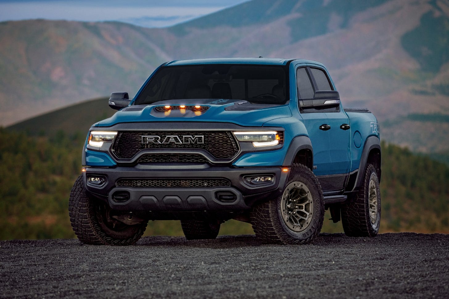 A blue 2024 Ram TRX Final Edition is parked on gravel in the mountains.