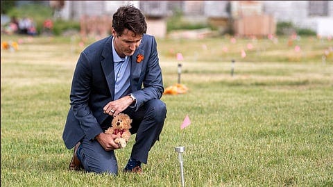 Justin Trudeau in a cemetery near a residential school holding a teddy bear