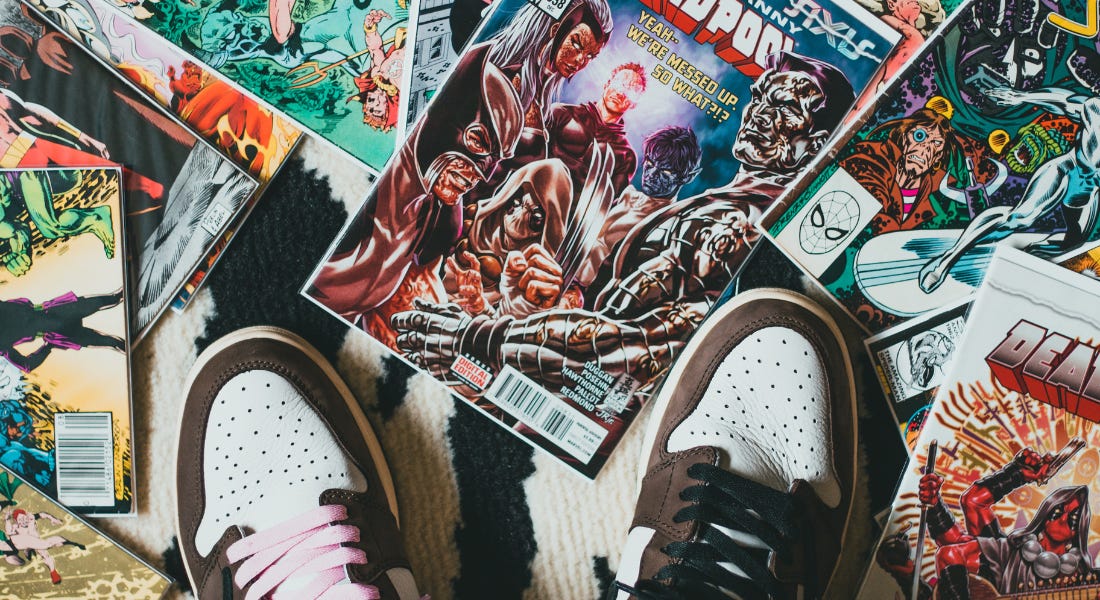 A birds eye view of two trainer feet on top of a carpet filled with comic books