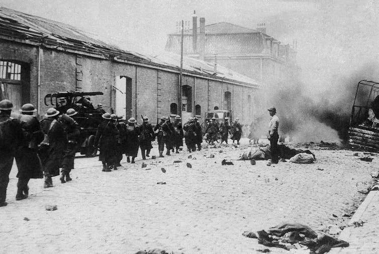 Troops marching along a street that has smoke rising at the end. Troops marching along a street that has smoke rising at the end.