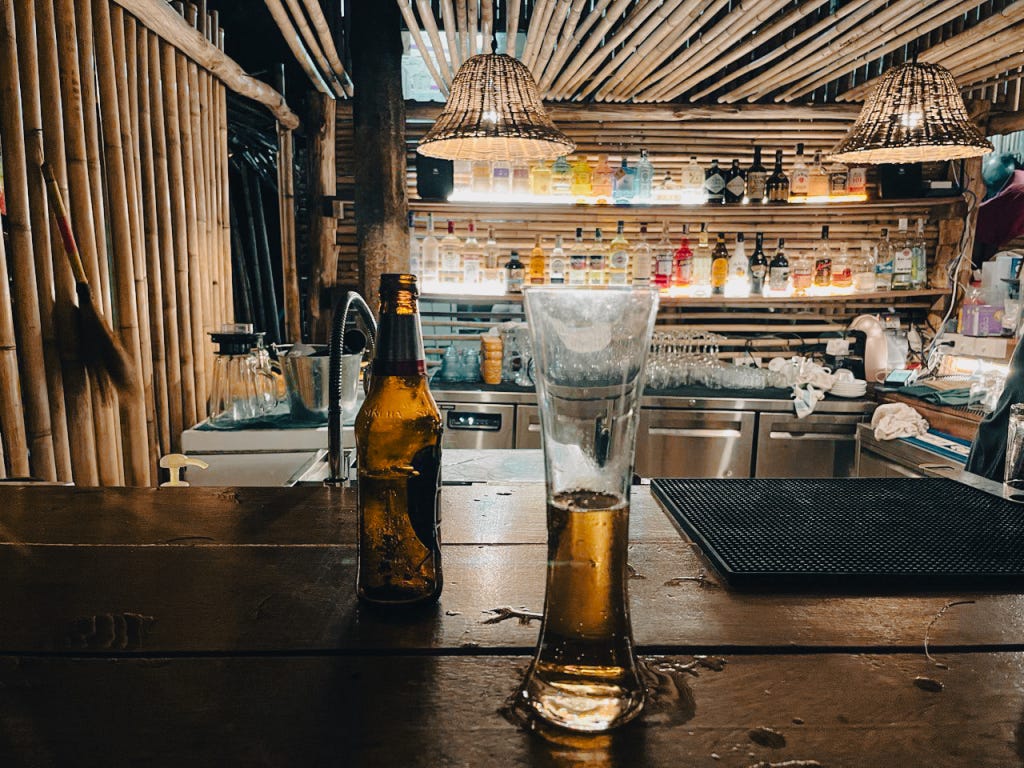 Quán bar bên bãi biển Bang Tao, một buổi chiều xẩm tối cuối tháng sáu, trời nổi cơn mưa, gió lạnh thổi vào từ Ấn Độ Dương, khách khứa quây quần lại trong quầy bar Quán bar bên bãi biển Bang Tao, một buổi chiều xẩm tối cuối tháng sáu, trời nổi cơn mưa, gió lạnh thổi vào từ Ấn Độ Dương, khách khứa quây quần lại trong quầy bar