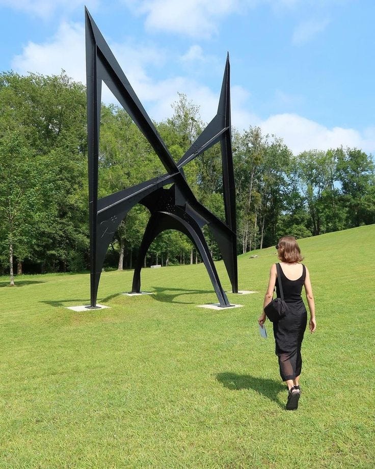 This may contain: a woman walking past a sculpture in the middle of a field