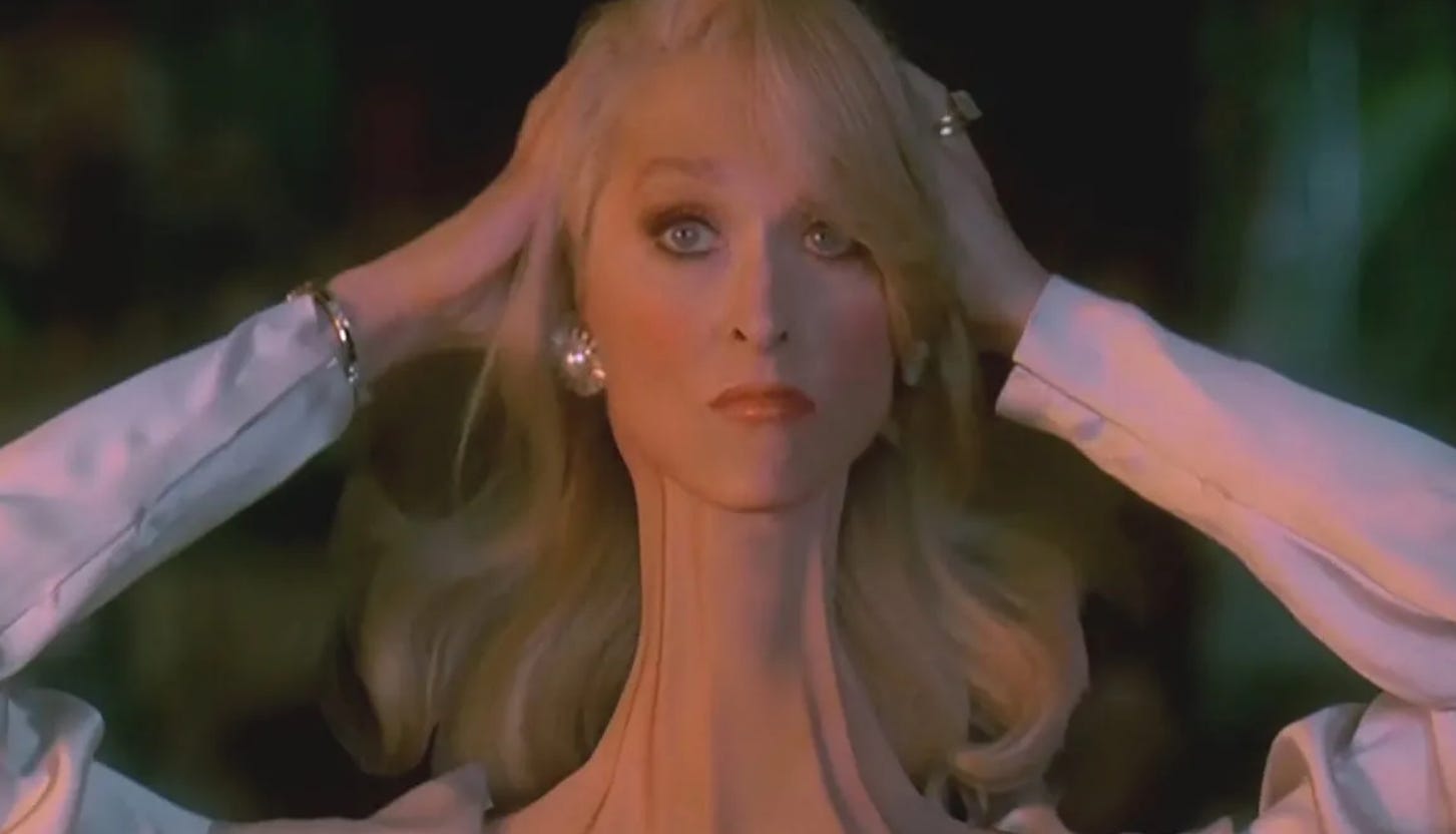 Cena do filme A morte lhe cai bem, em que a Meryl Streep aparece com o pescoço longo e todo retorcido. Ela segura a cabeça com as duas mãos.