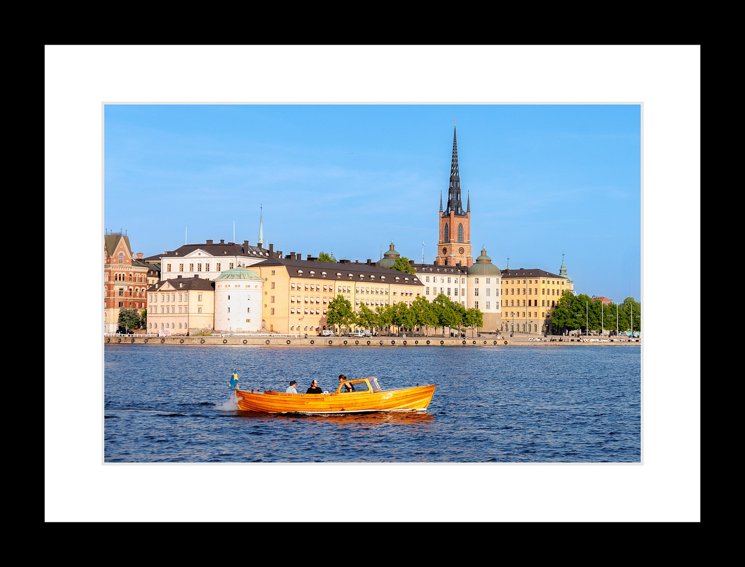 Boat cruising in Stockholm harbor with historic buildings and a church spire in background.
