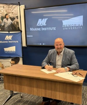 Dr. Paul Brett signs MOU. smiling at camera with pen in hand