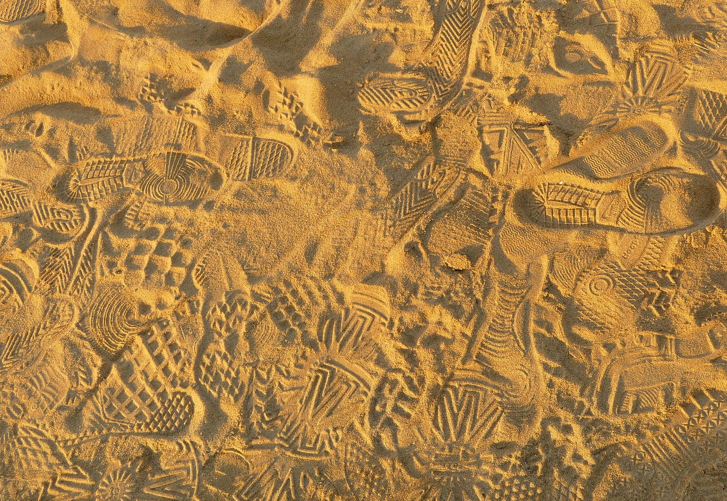 Sand marked by many varying bootprints Sand marked by many varying bootprints