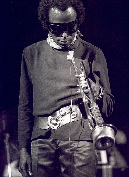 This may contain: a man wearing sunglasses and holding a saxophone in his right hand while standing next to a microphone