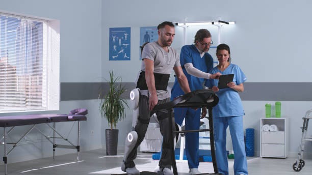 Doctors discussing rehabilitation results near patient in exoskeleton Male and female rehabilitation therapists talking and analyzing data on tablet near man in exoskeleton walking on treadmill in futuristic clinic Tele rehabilitation stock pictures, royalty-free photos & images