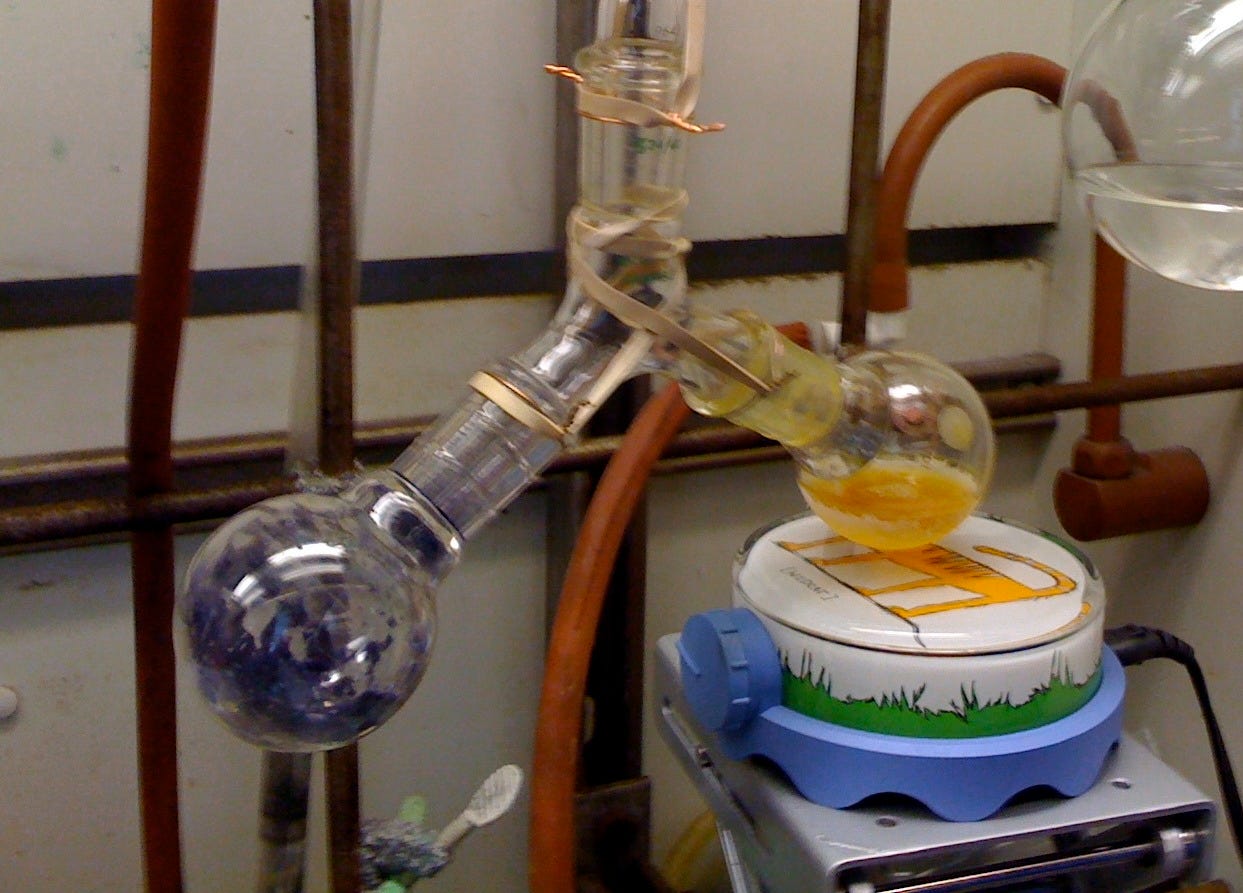 Picture of a scientific apparatus. One flask has purple powder. The other flask has orange powder. The two flasks are connected via a y-shaped glass connector.