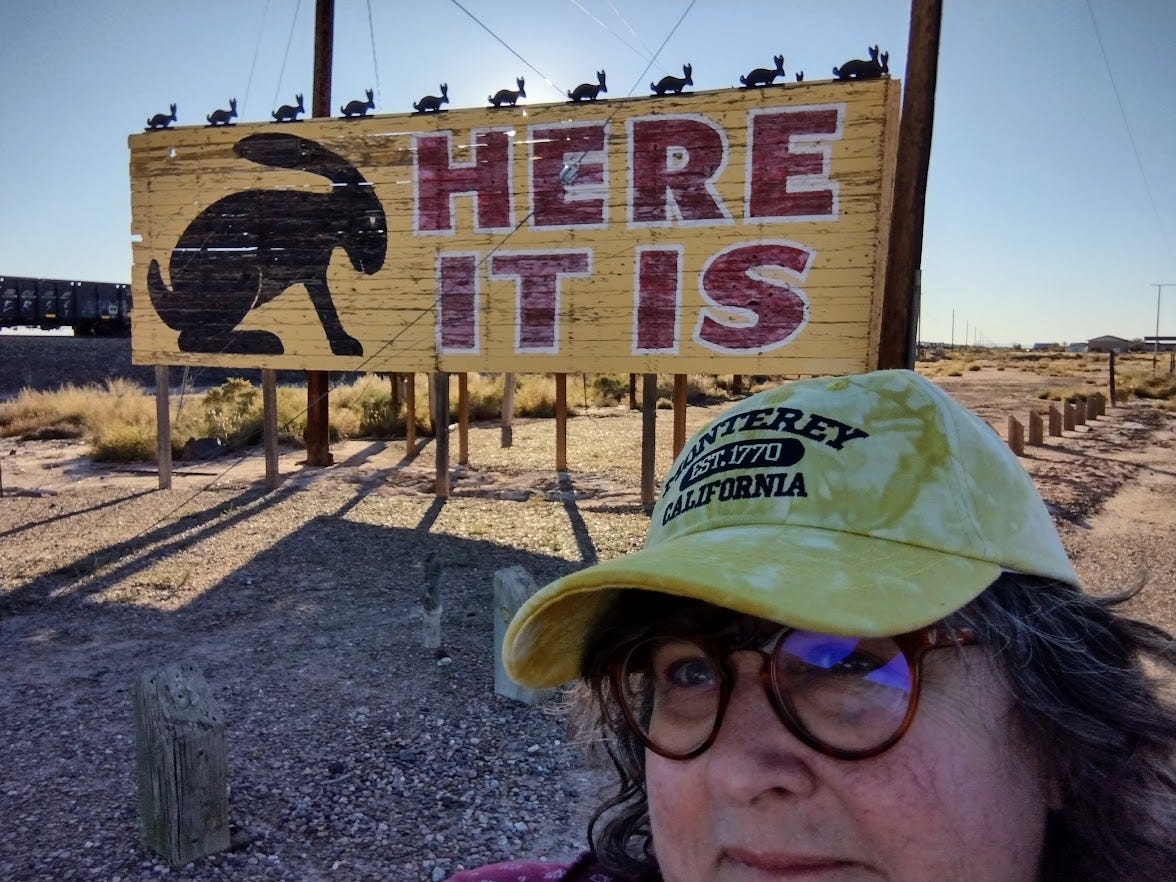 woman in front of billboard featuring rabbit silhouette and words Here It Is