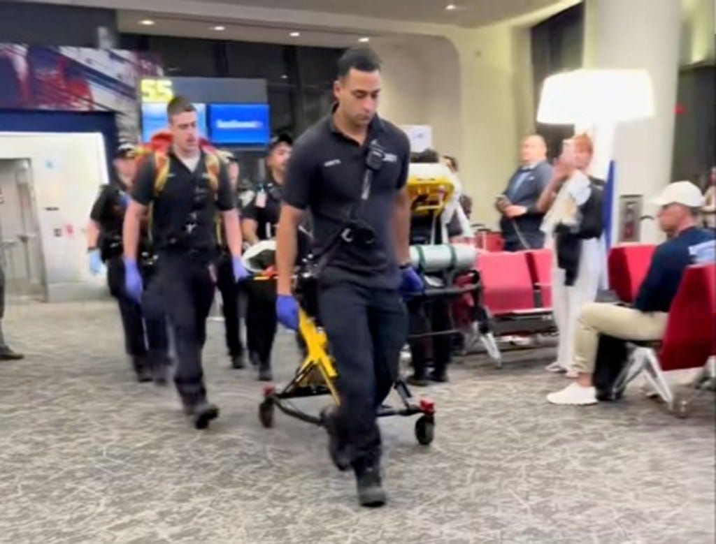 A restrained passenger being wheeled out of an airport on a stretcher.