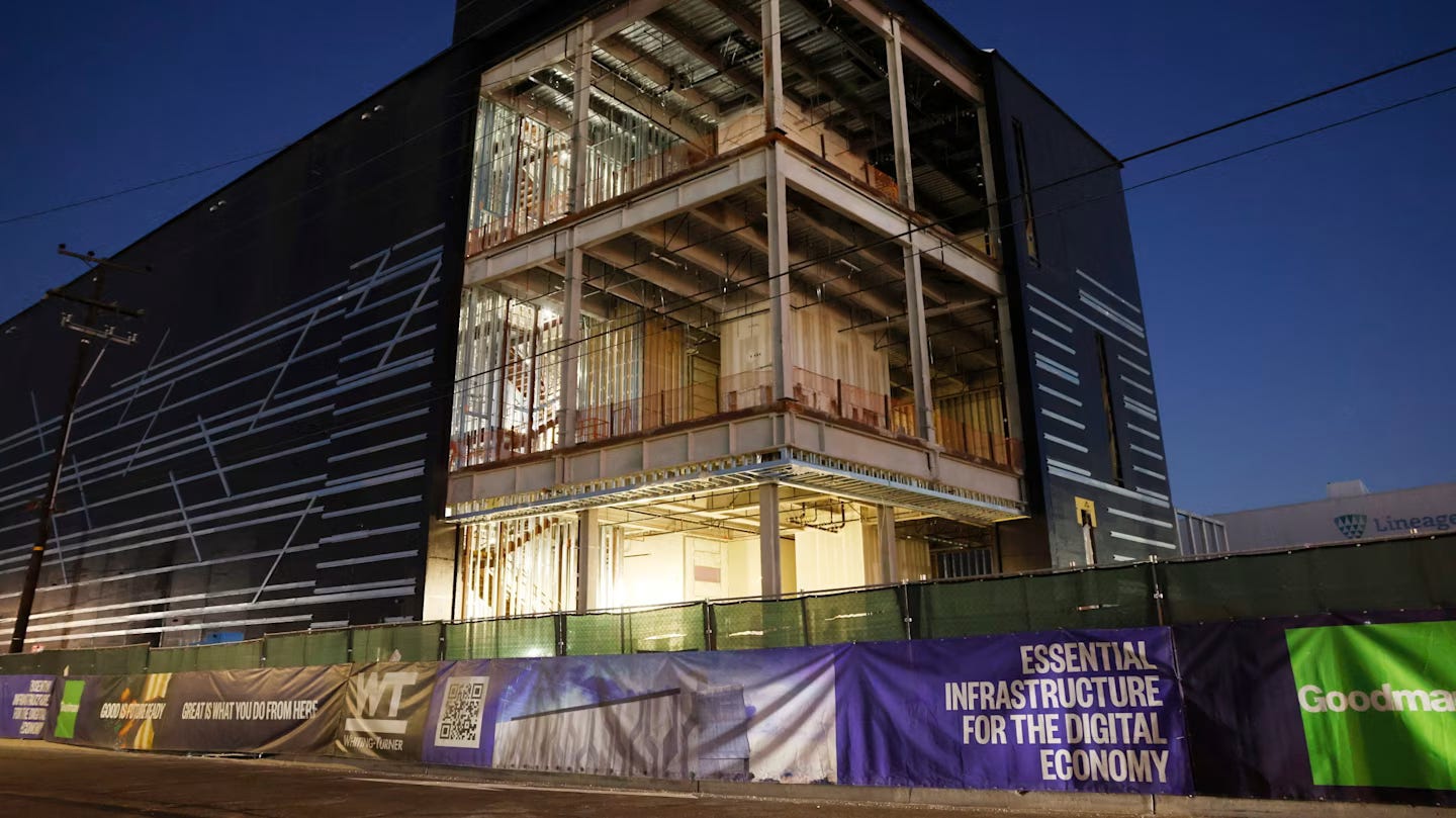 A large three-level data centre under construction in California is seen at night, with illuminated interior framing and banners promoting digital infrastructure. A large three-level data centre under construction in California is seen at night, with illuminated interior framing and banners promoting digital infrastructure.