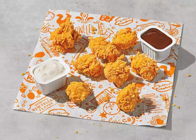 A portion of chicken nuggets and two containers of dipping sauce arranged on a piece of paper with Popeyes branding