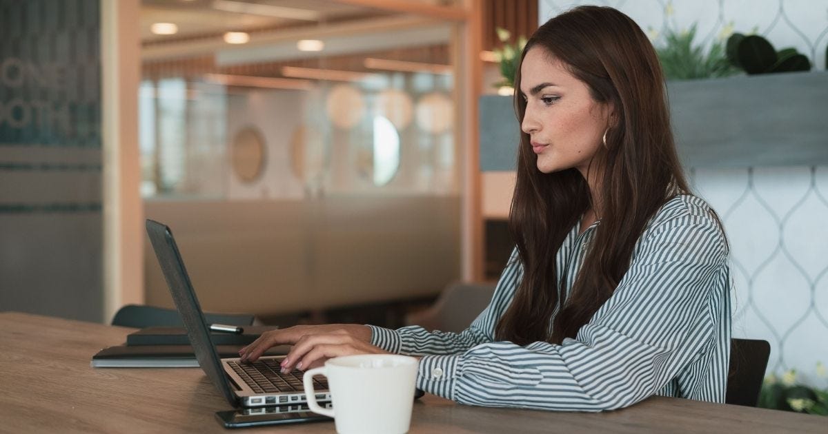 A professional woman working on her laptop at a modern office with a coffee cup nearby A professional woman working on her laptop at a modern office with a coffee cup nearby