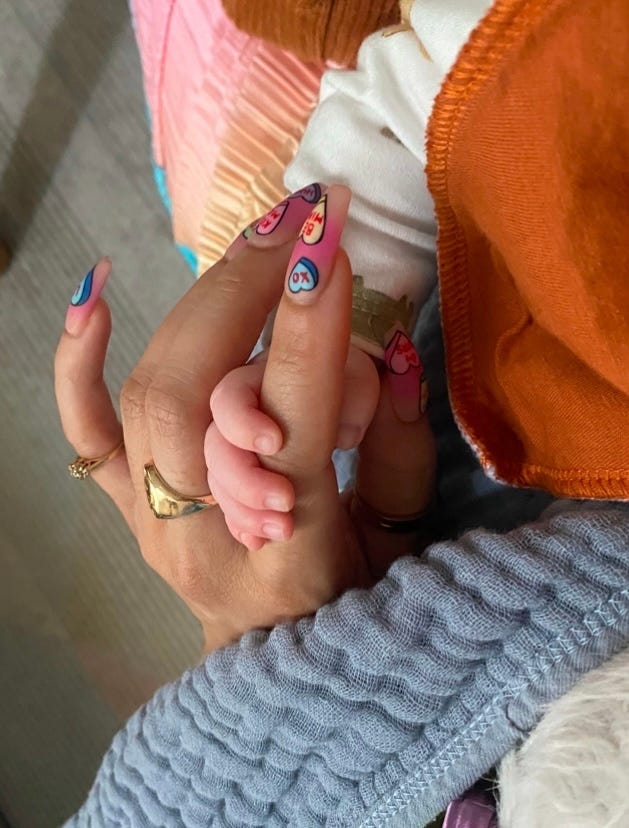 A tiny white baby hand gripping Kiana's tan finger with her presson on.