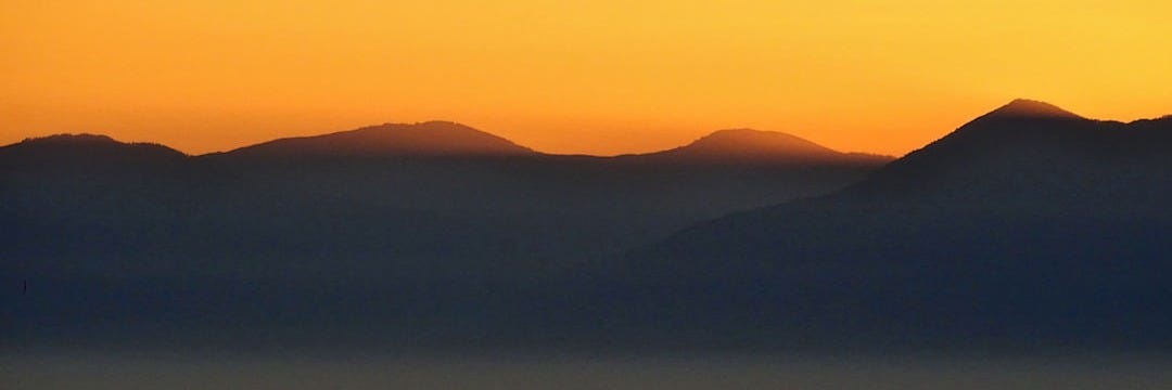 the sun is setting over the mountains in the distance the sun is setting over the mountains in the distance