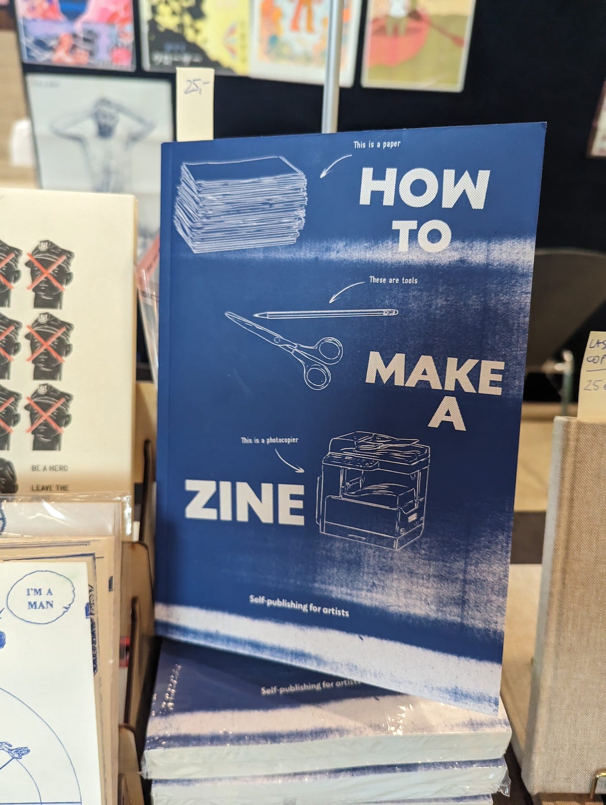 Cover of How to Make a Zine, a guide for self-publishing artists, featuring a minimalist blue and white design with illustrations of paper, scissors, a pen, and a photocopier.